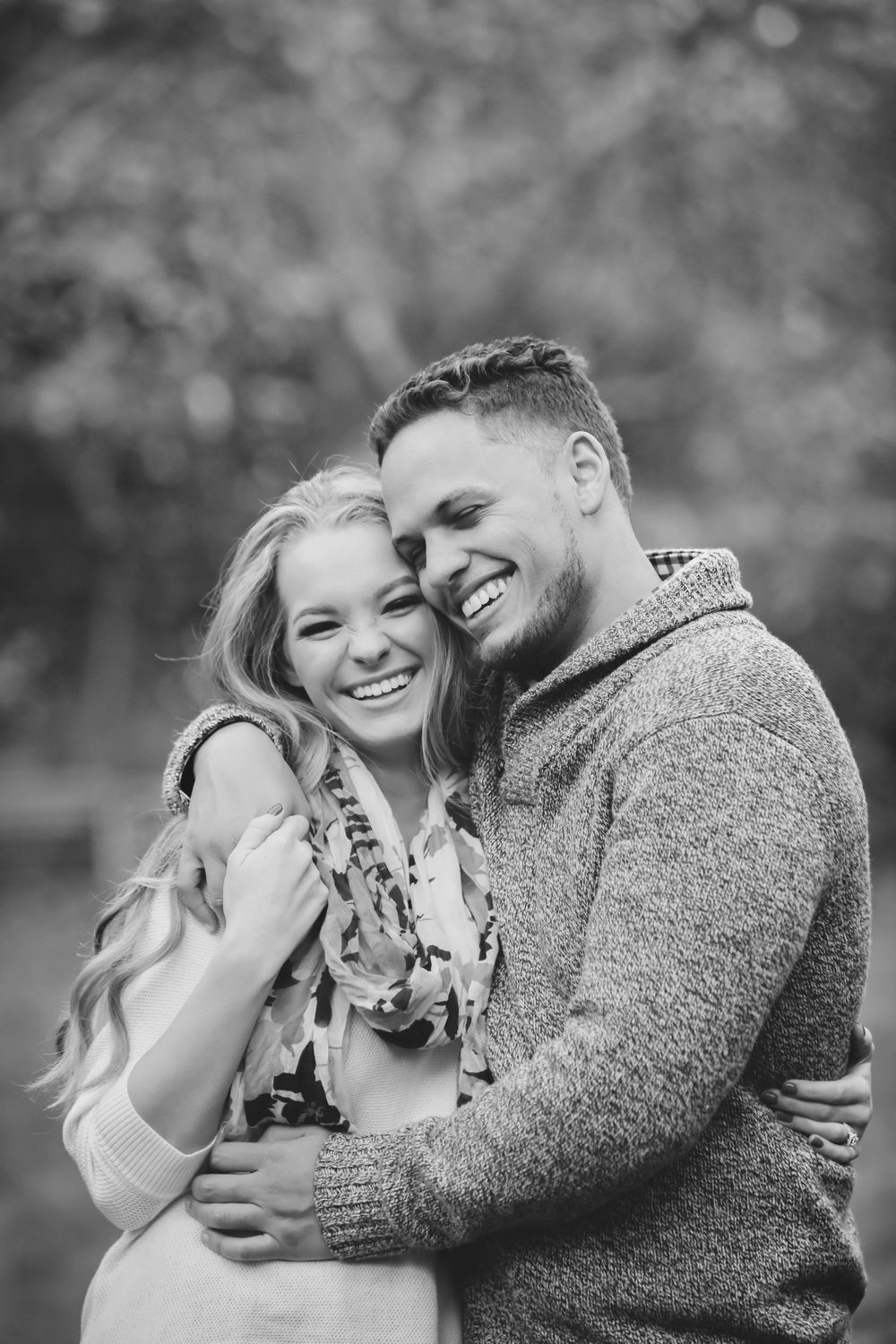 Black and white romantic portrait of a couple embracing and laughing together outdoors in casual sweaters.