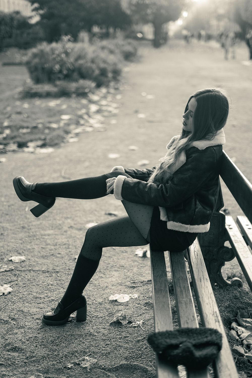 Black and white image of person lounging on park bench in vintage style clothing and high heels.