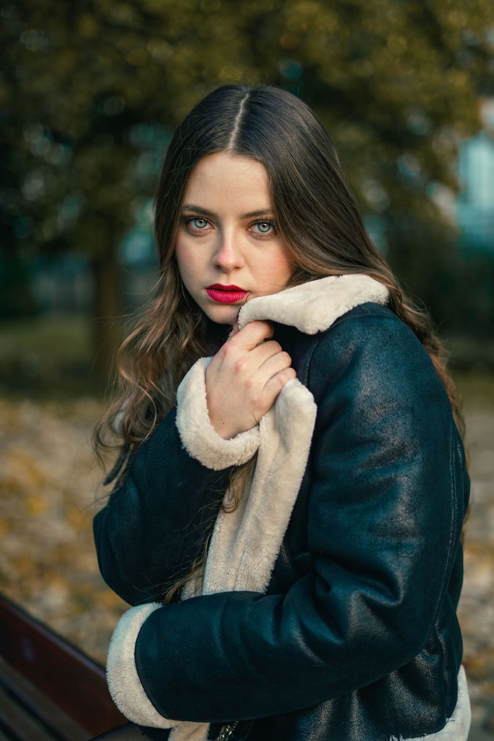 Winter fashion portrait of woman in dark shearling coat against blurred outdoor background.