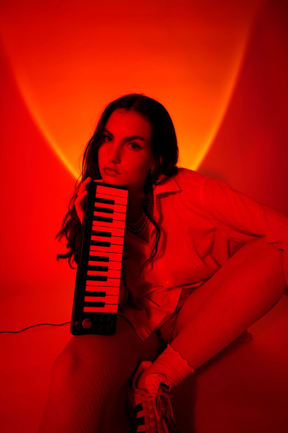 Artistic portrait in red lighting showing musician with MIDI keyboard in moody atmosphere.