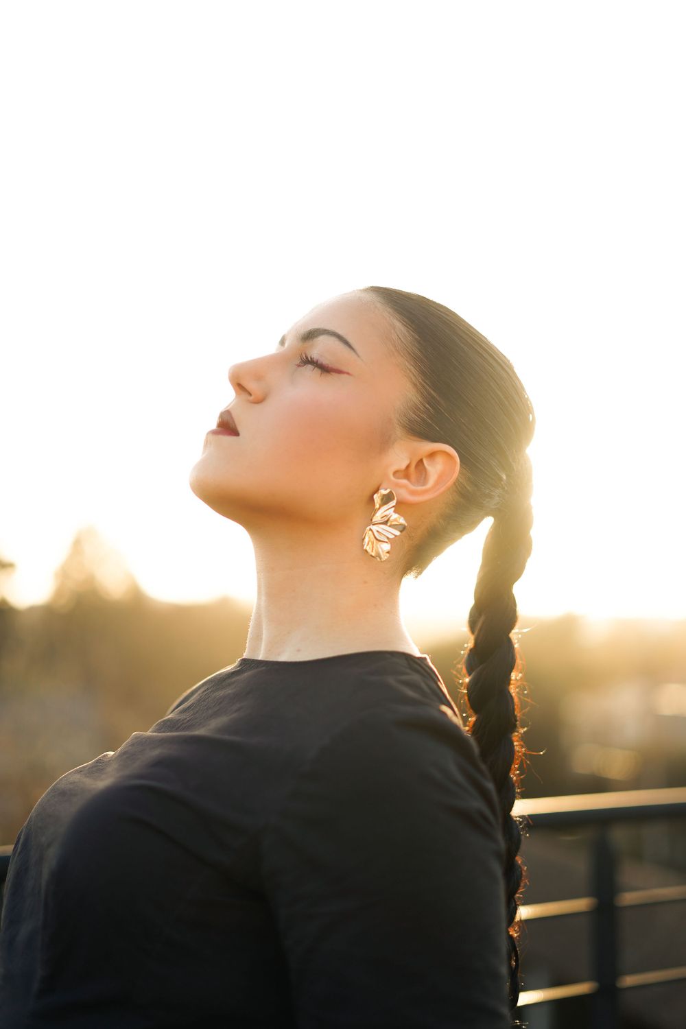 Silhouette of a woman with braided hair and earrings in profile against a golden sunset background.