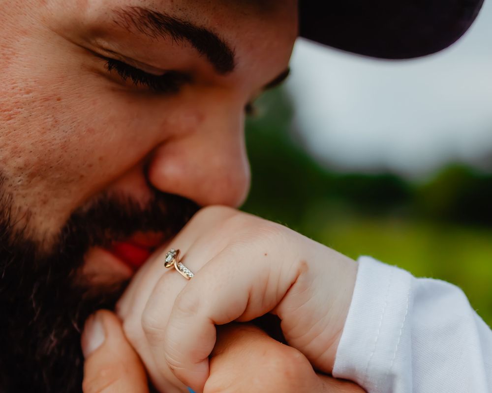 Close up of someone wearing a wedding ring and white shirt sleeve against a green outdoor background.