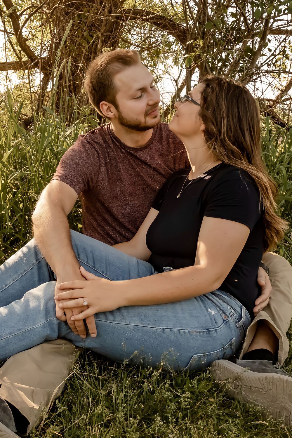 Couple in casual attire sharing an intimate moment while sitting in tall grass during golden hour.