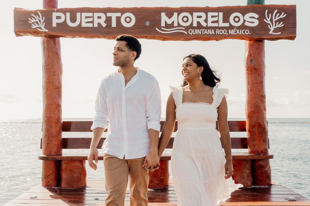 Couple posing under Puerto Morelos sign on wooden pier at sunset photoshoot in Puerto Morelos.