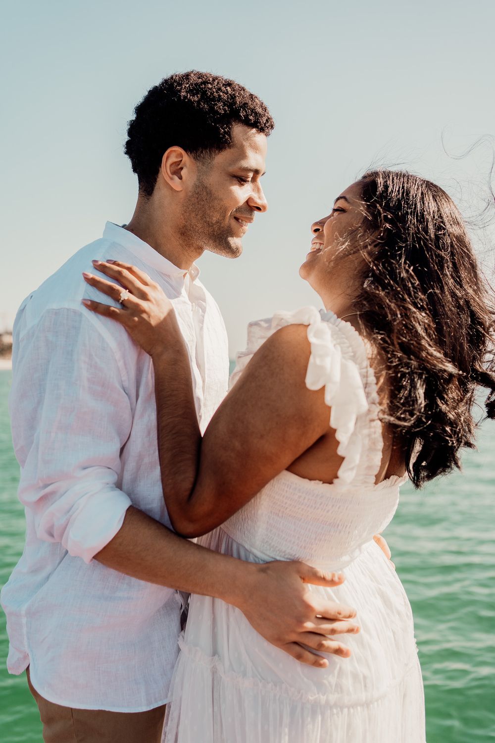Romantic couple embracing by turquoise waters in white summer outfits photoshoot in Puerto Morelos.