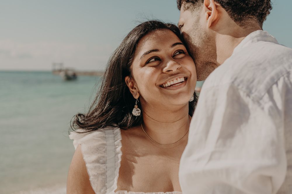 Romantic couple sharing intimate moments on a sunny beach with blue ocean in the background photoshoot in Puerto Morelos.