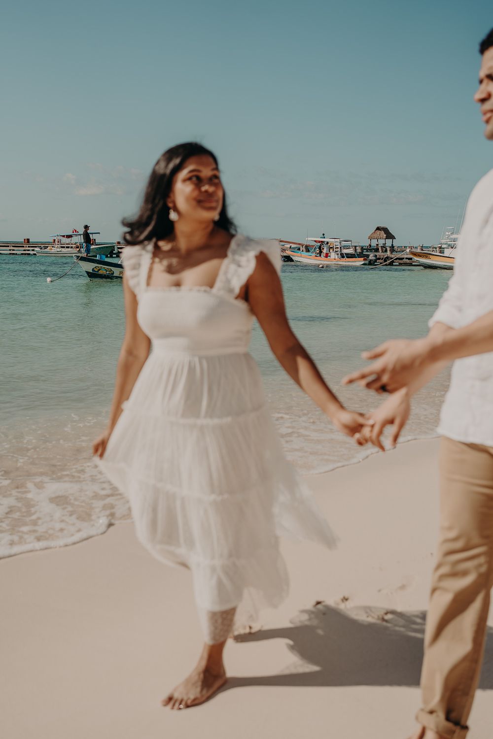 Person in a flowing white dress twirling joyfully on a sandy beach photoshoot in Puerto Morelos.