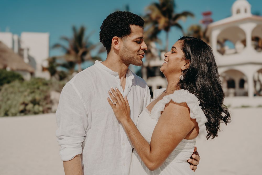 Couple embracing on tropical beach with palm trees and colonial architecture visible photoshoot in Puerto Morelos.