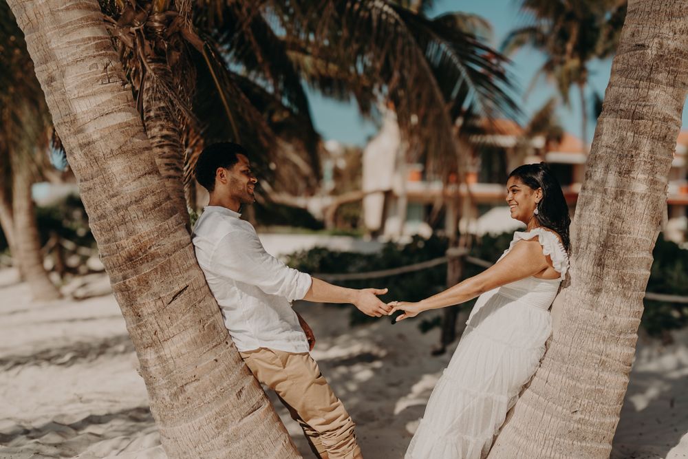 Couple sharing romantic moments between palm trees on a sunny beach photoshoot in Puerto Morelos.