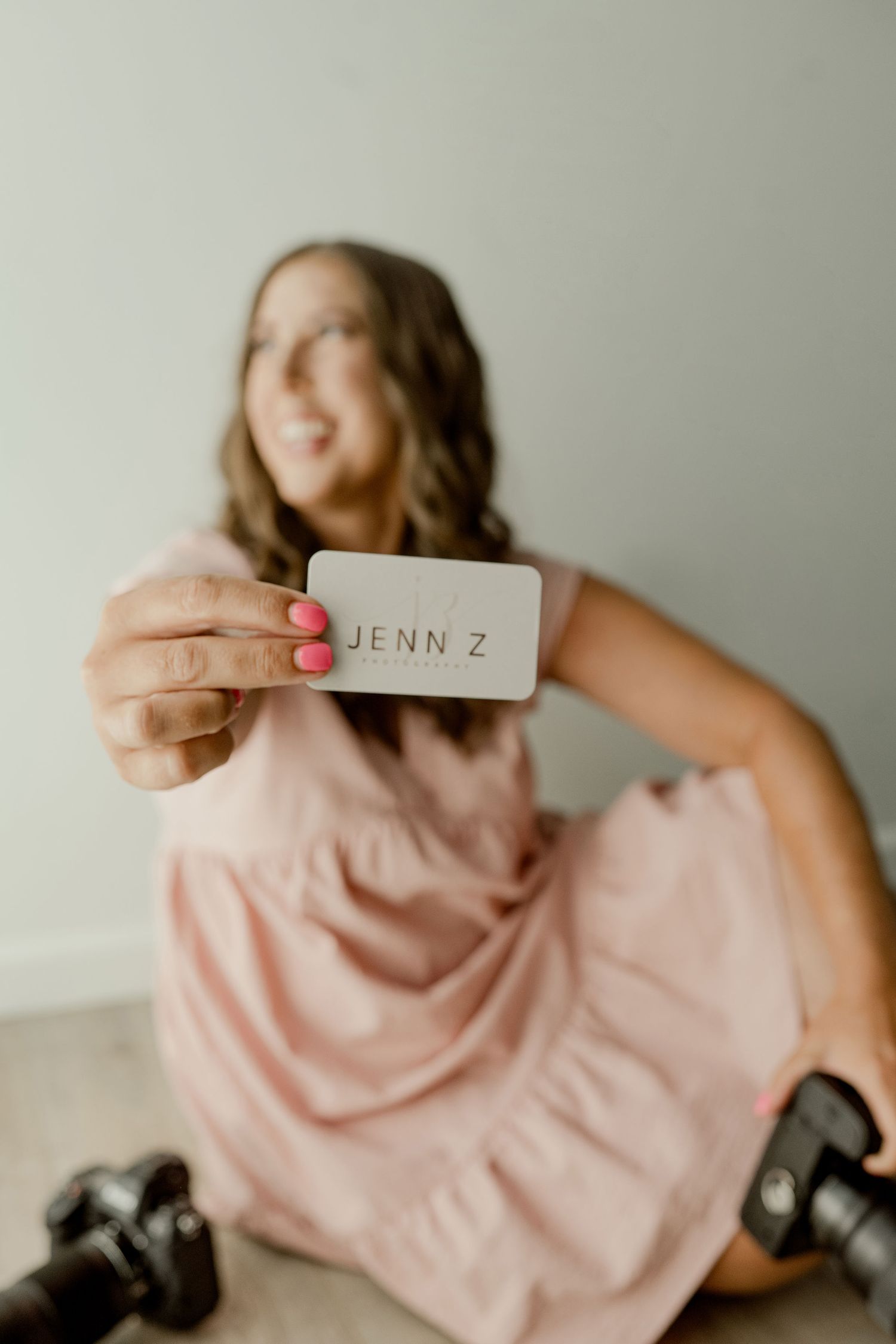 Professional photographer in pink dress poses with camera and name card.