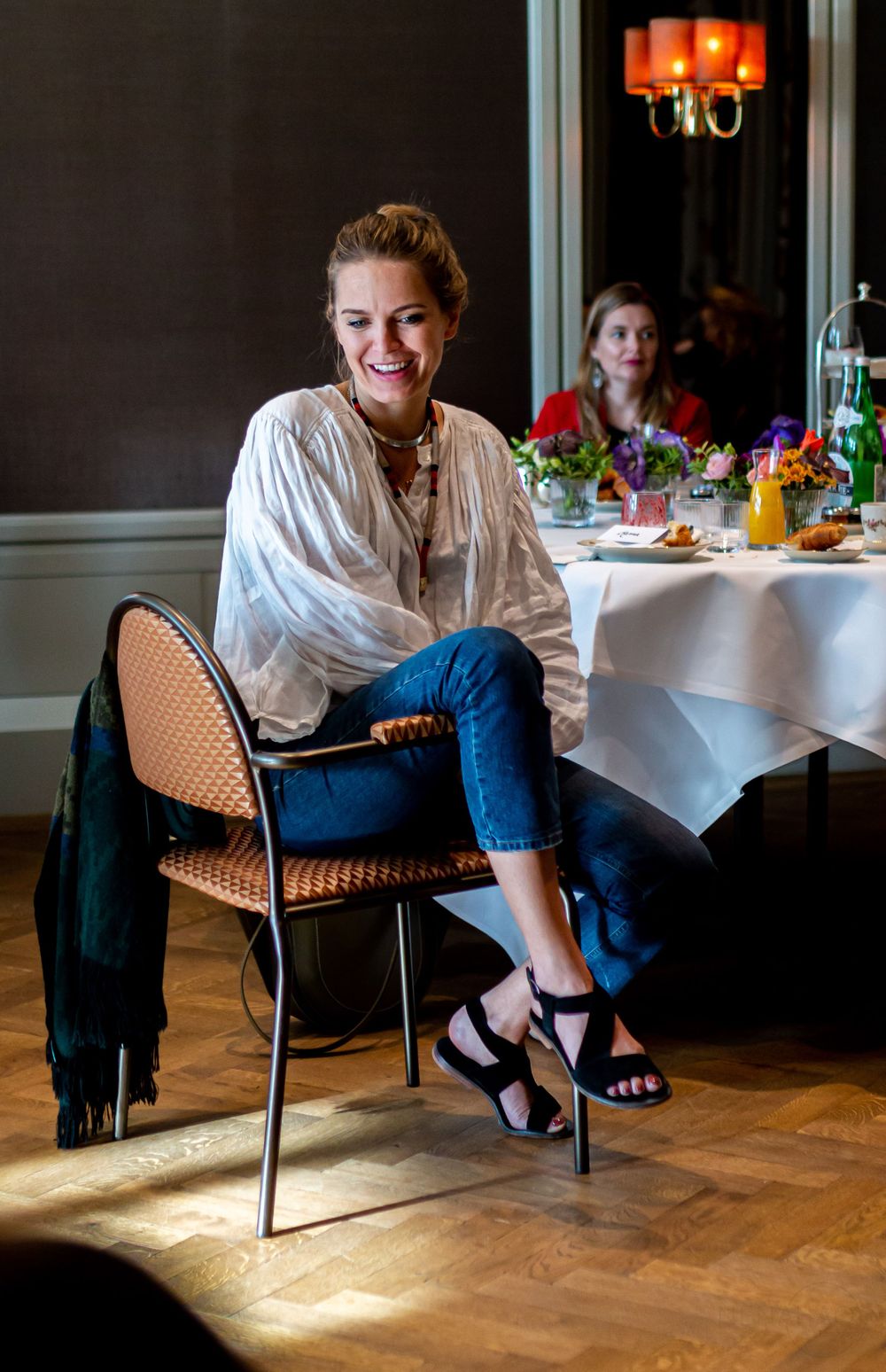 Person in white shirt and jeans seated at an elegant restaurant table with sunlight streaming in.