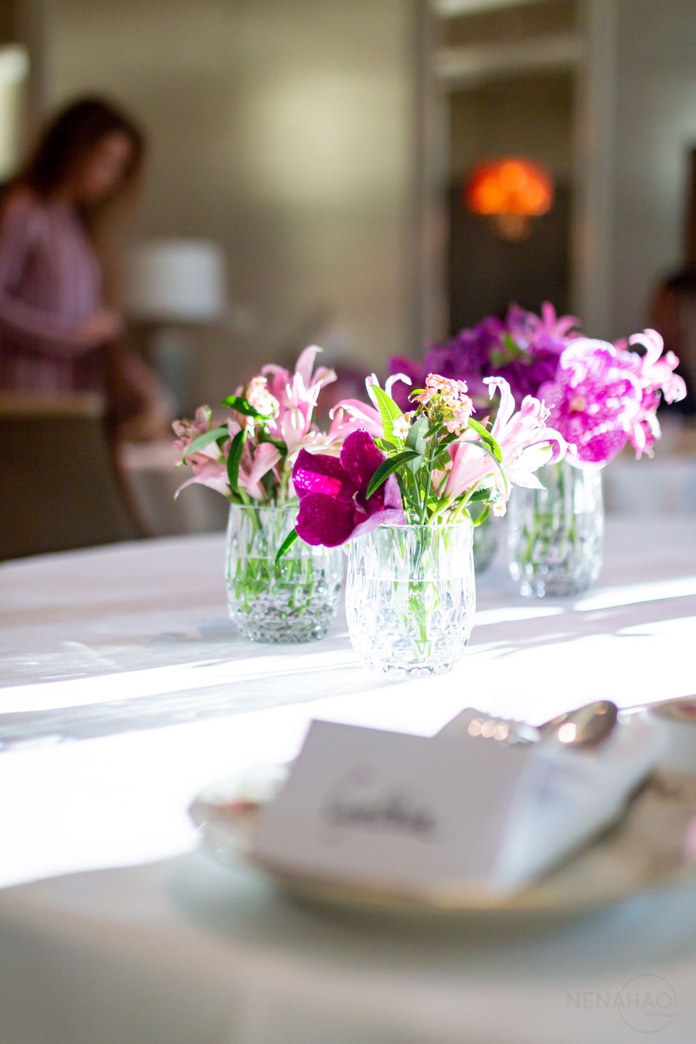 Close-up of pink and white flower arrangements in crystal vases on white tablecloth.