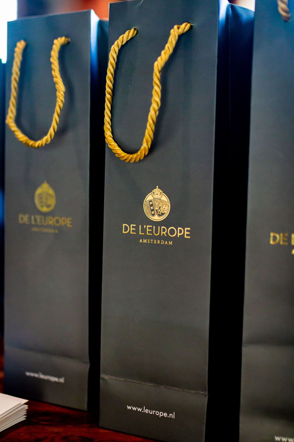 Row of black shopping bags with gold handles and 'De L'Europe' branding.