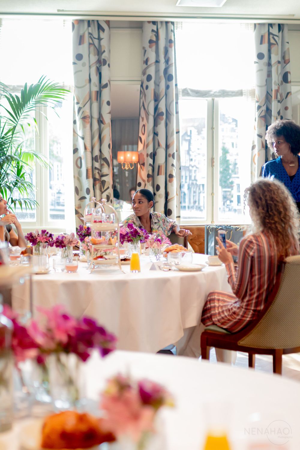 Elegant dining room setup with white tablecloths and pink floral centerpieces near windows.