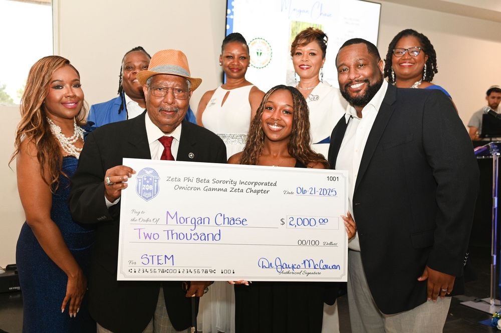A group of people pose together while holding a large ceremonial check at an awards or presentation ceremony.