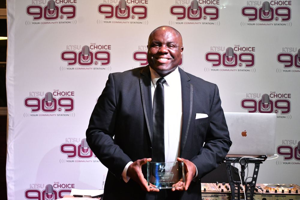 An award winner holds a trophy at a red carpet event with Choice 909 backdrop.