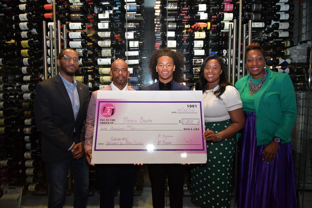 Team members posing with oversized presentation check in front of wine rack display.