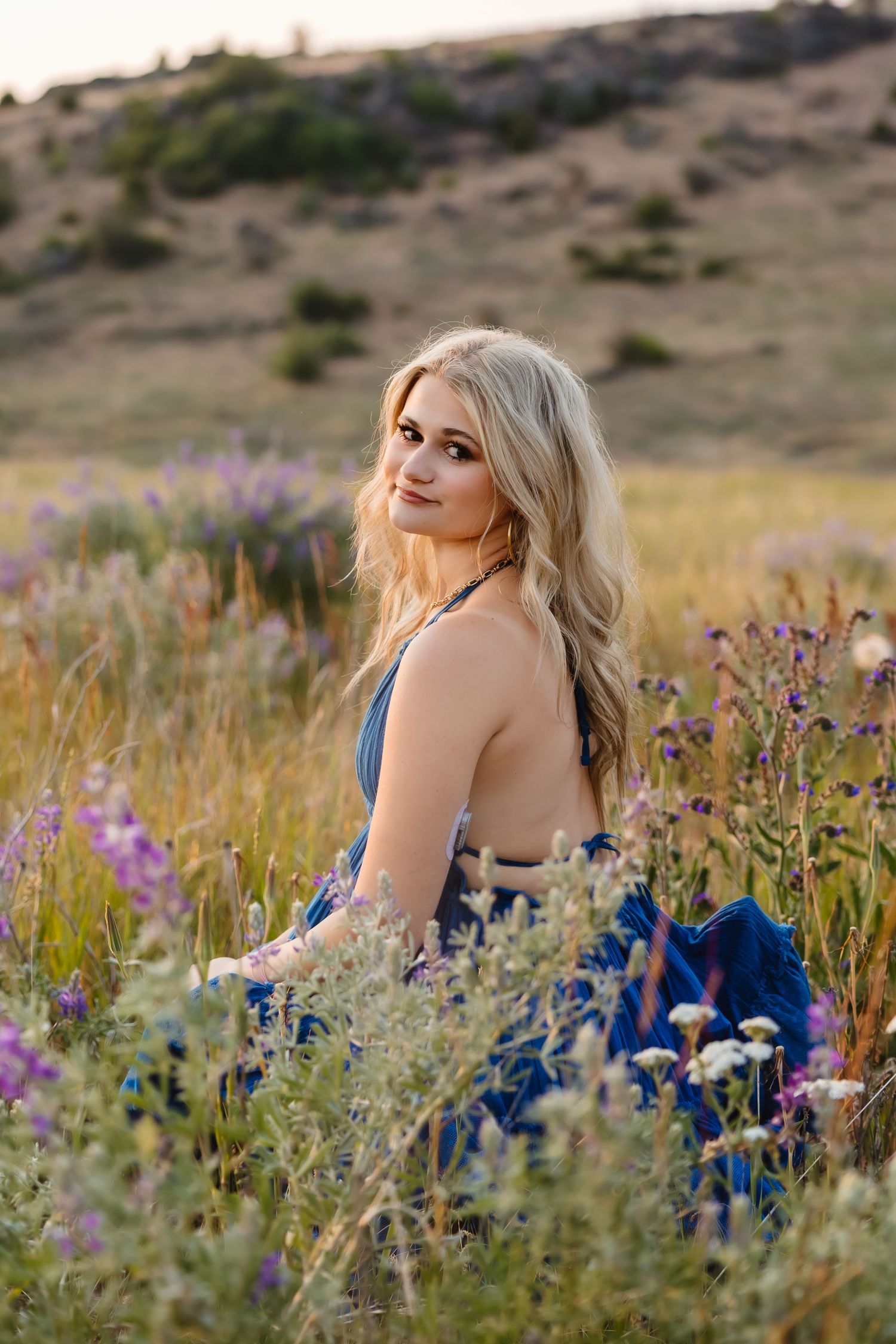 A person wearing a white sleeveless top and jeans stands in a sunlit meadow with golden grass and trees in the background.