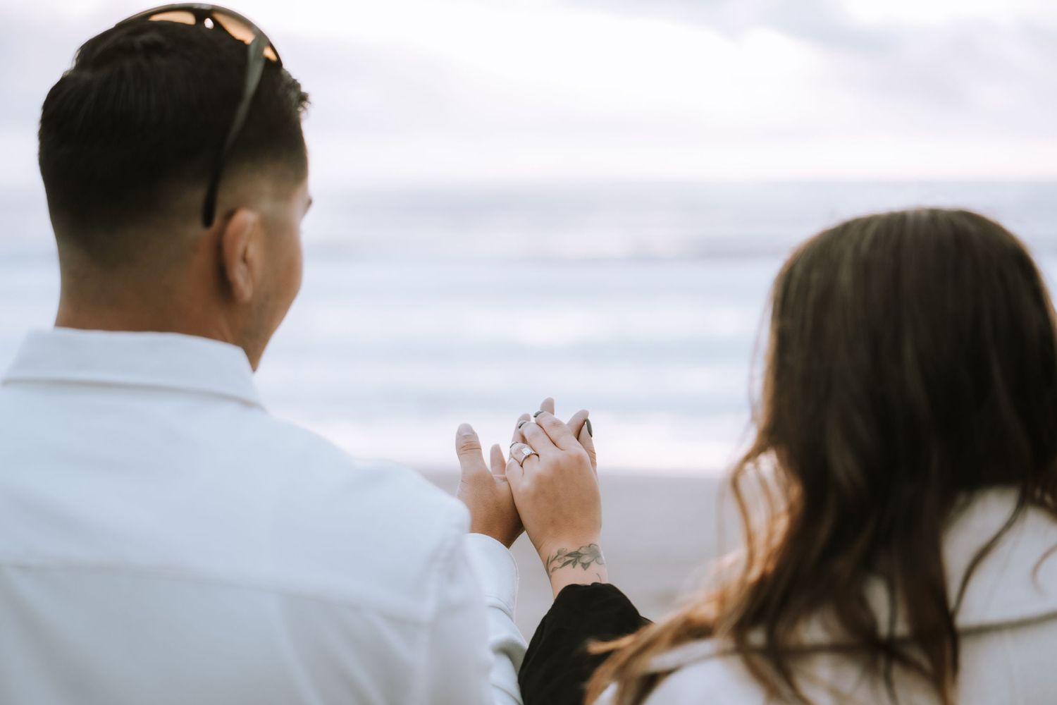 Two people enjoying hot drinks together while looking at an ocean view on an overcast day.