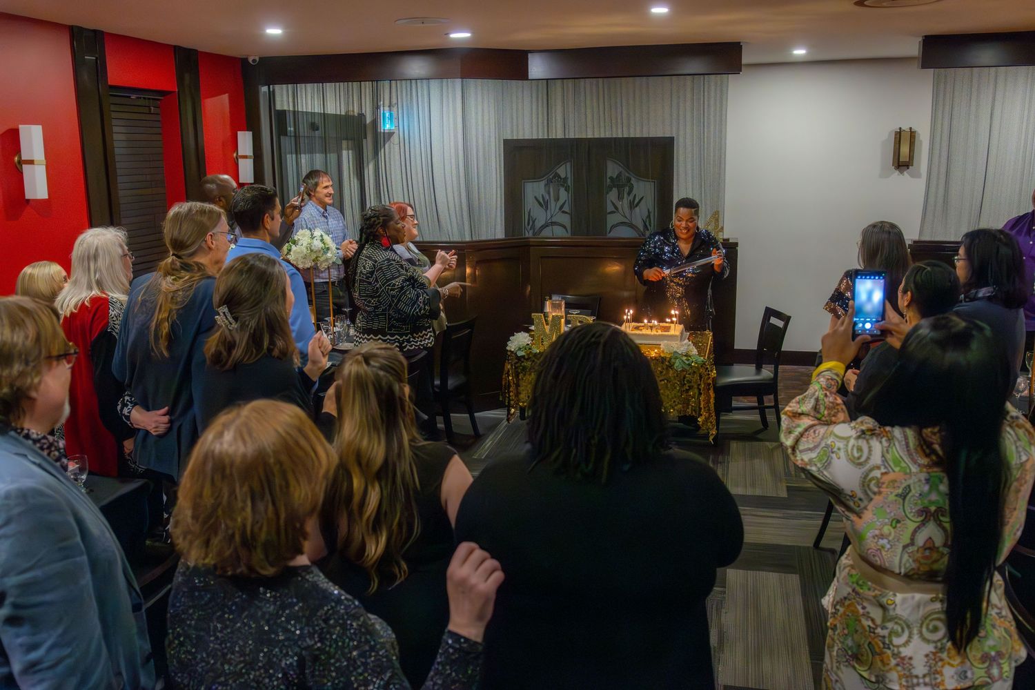 A crowd of people gather around a piano in a dimly lit room during what appears to be a musical performance.