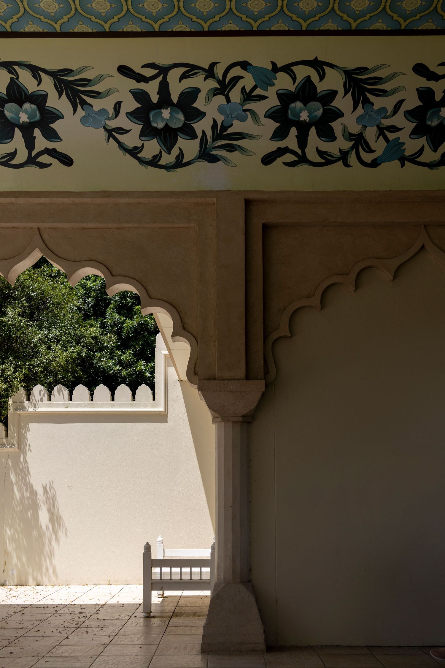 Ornate archway with floral patterns and scalloped plaster details, partially shaded by overhanging greenery.