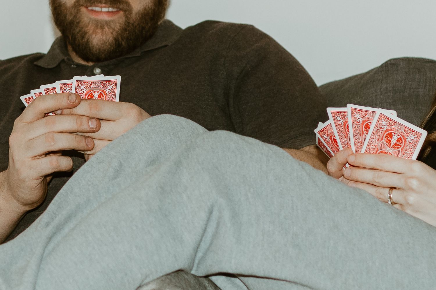 Person holding playing cards while relaxing on a couch during a casual card game.