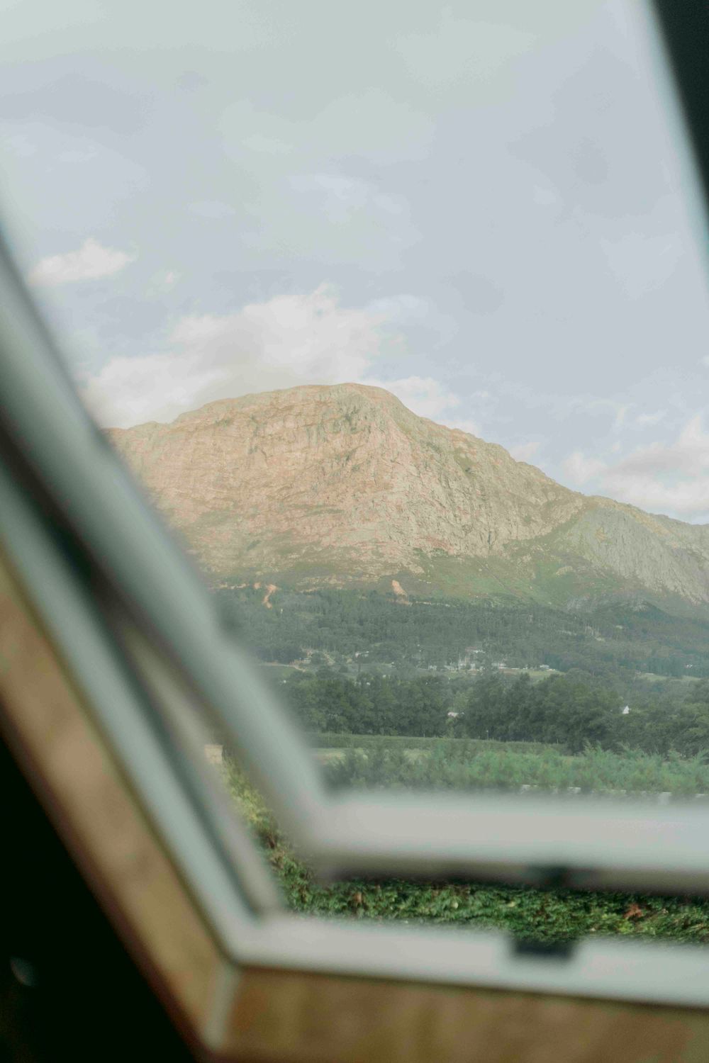 Scenic mountain view framed through a skylight window with lush green trees below.