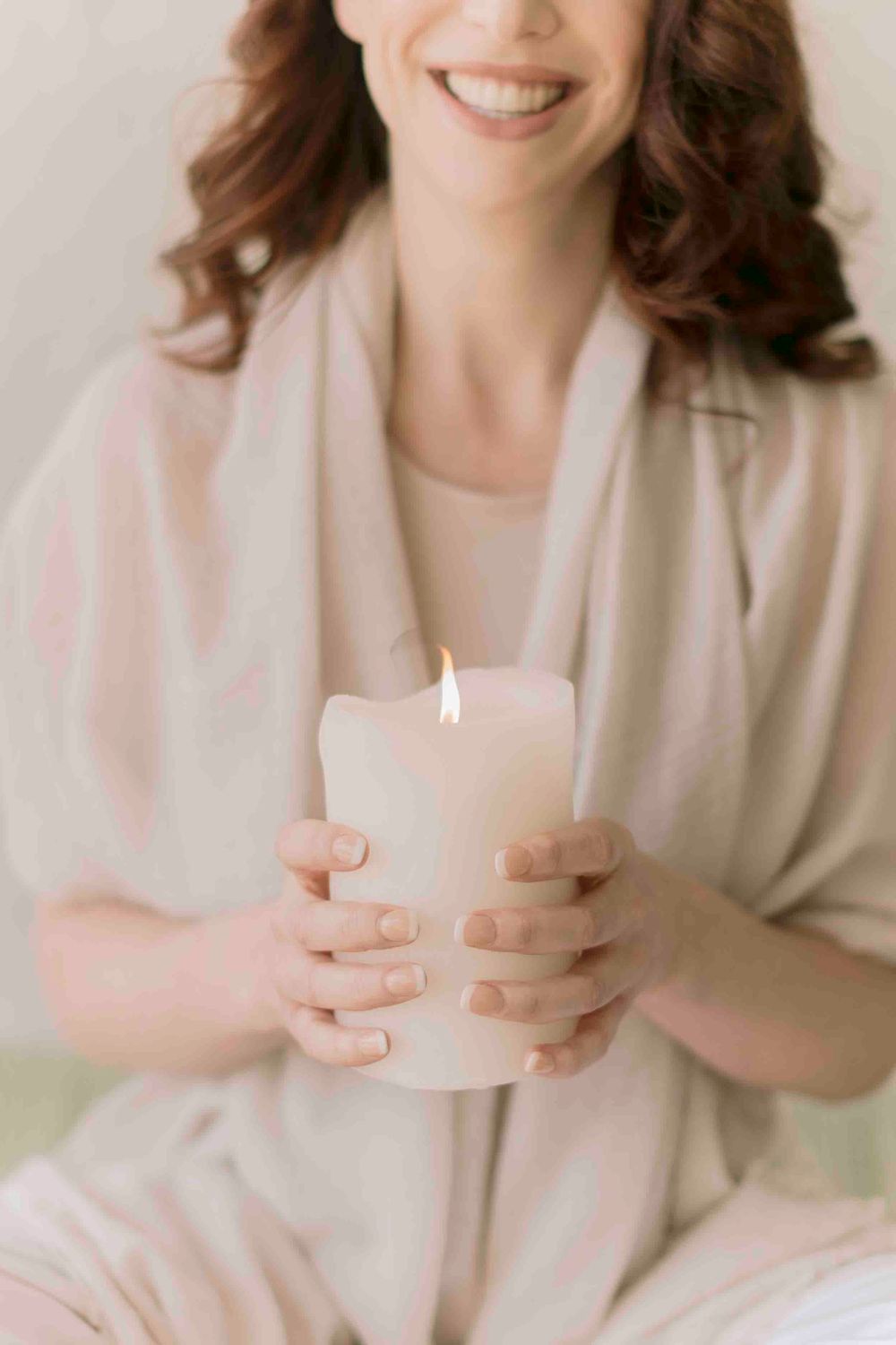 Smiling woman holding a glowing white pillar candle in a serene wellness and mindfulness setting.