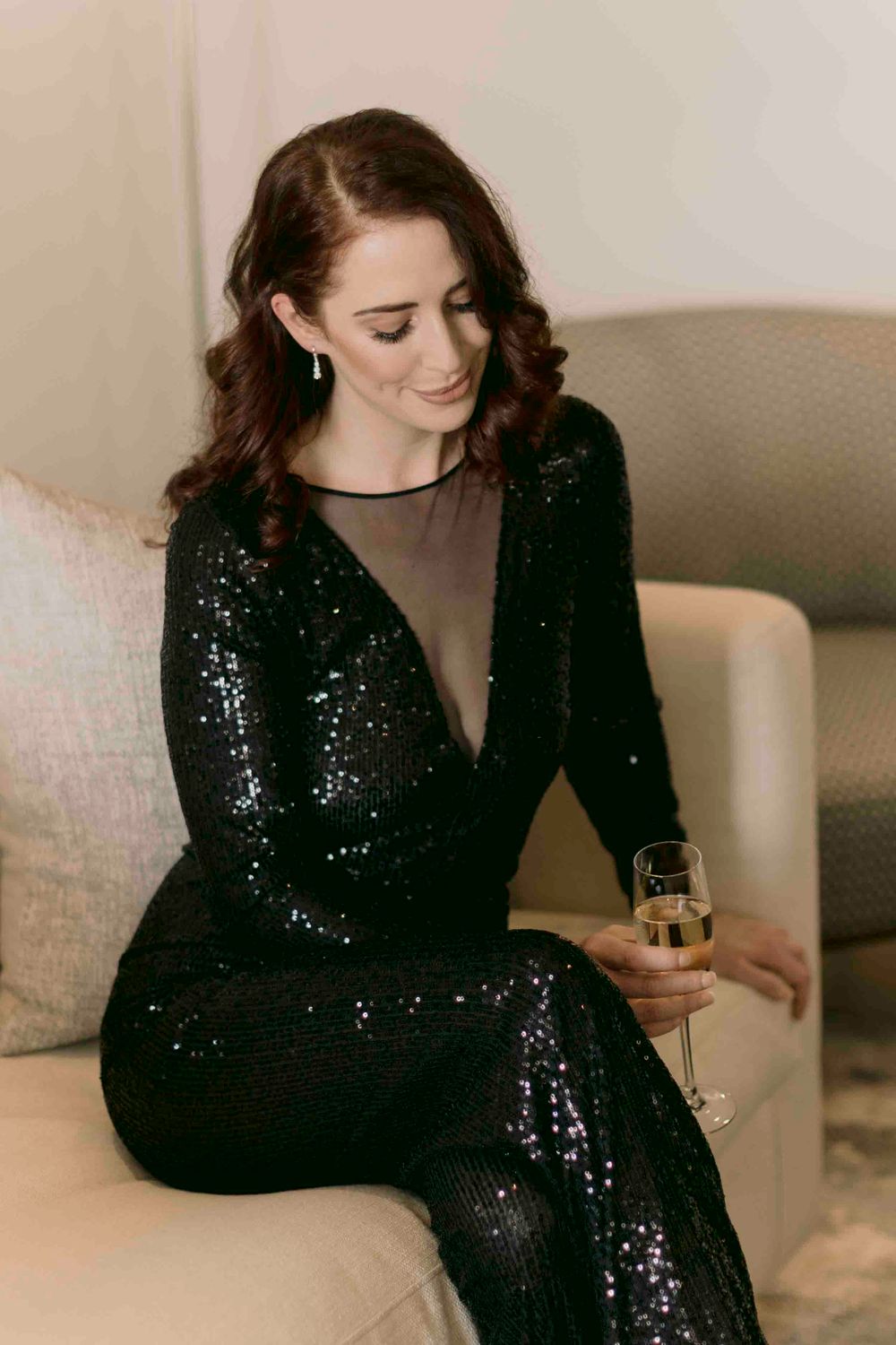 Elegant woman in black sequin dress holding a champagne glass while seated on a sofa.