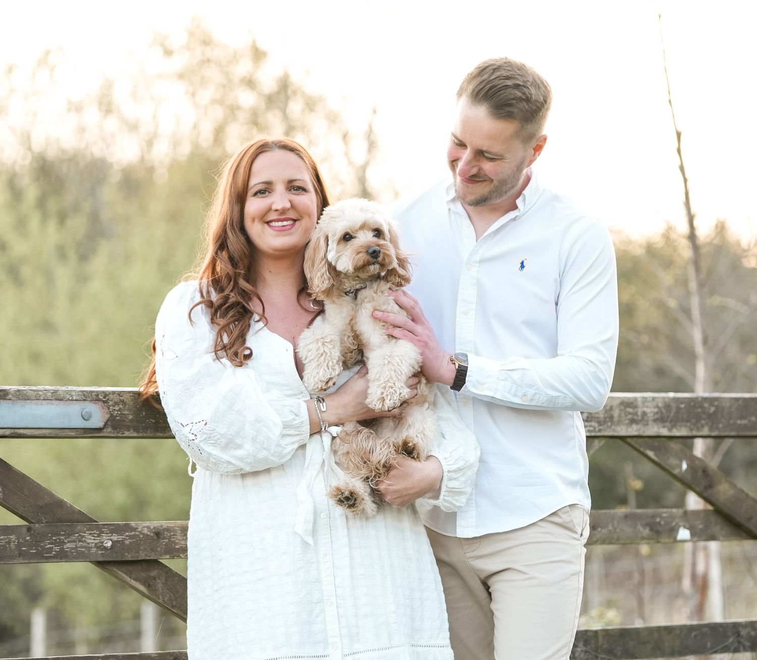 White-dressed couple holding small fluffy dog in outdoor setting.
