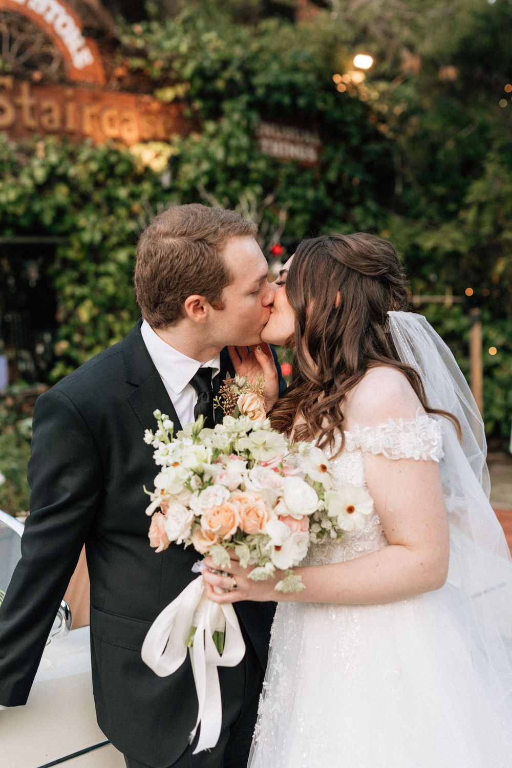 A bride and groom kiss in front of a vintage car for wedding photography in los angeles