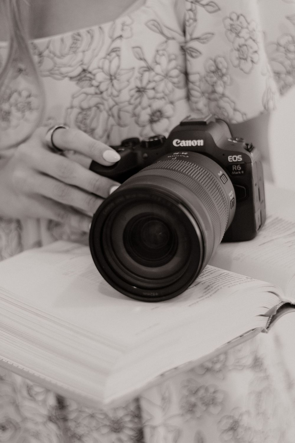 A Canon EOS camera with black lens sits on a white surface with floral patterns in the background.