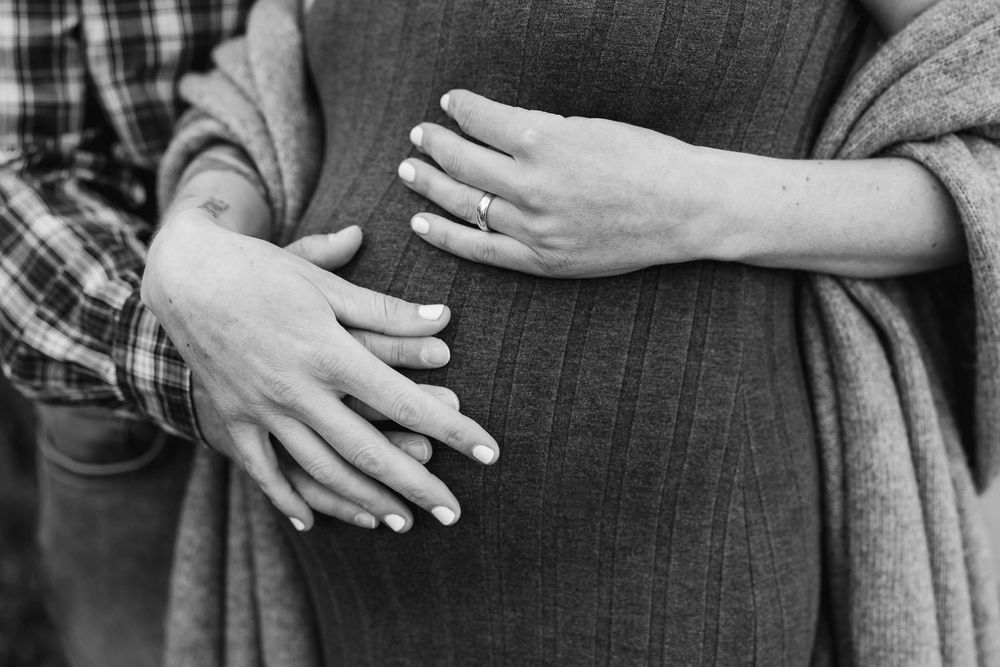 Black and white close-up of hands lovingly touching a pregnant belly, dressed in plaid and cozy sweater.