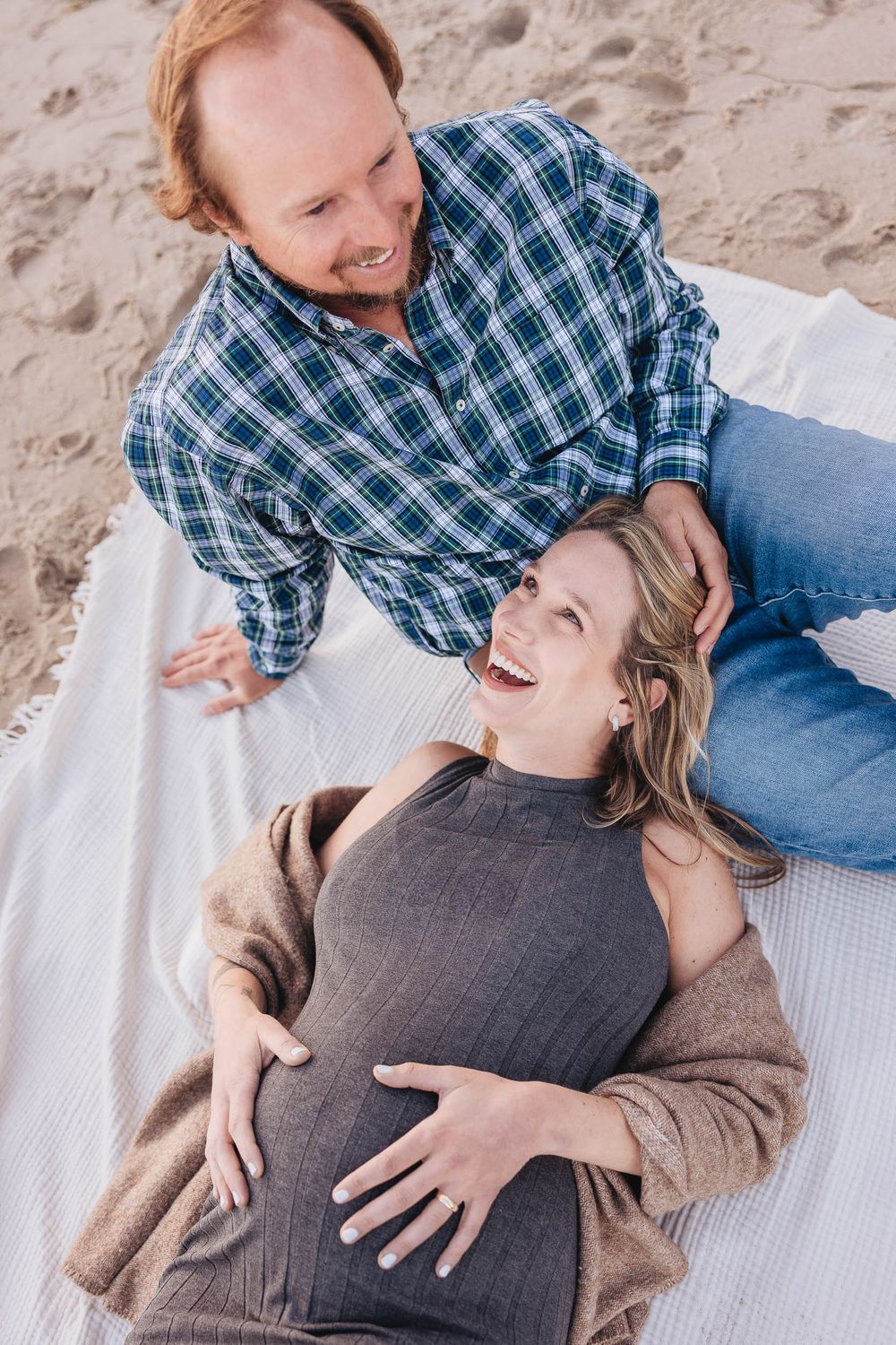 A couple lying on a white blanket on the beach share a joyful moment together.