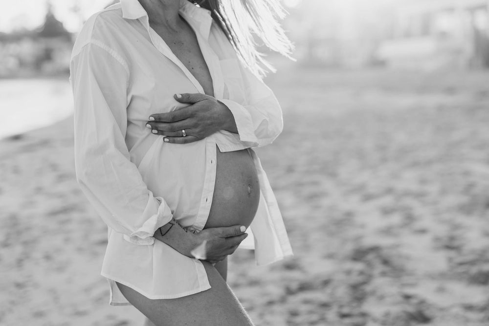 Black and white photo showing a pregnant silhouette against a beach backdrop.