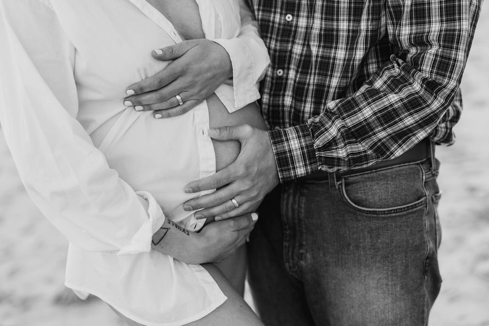 Close-up black and white photo of hands tenderly cradling a pregnant belly.