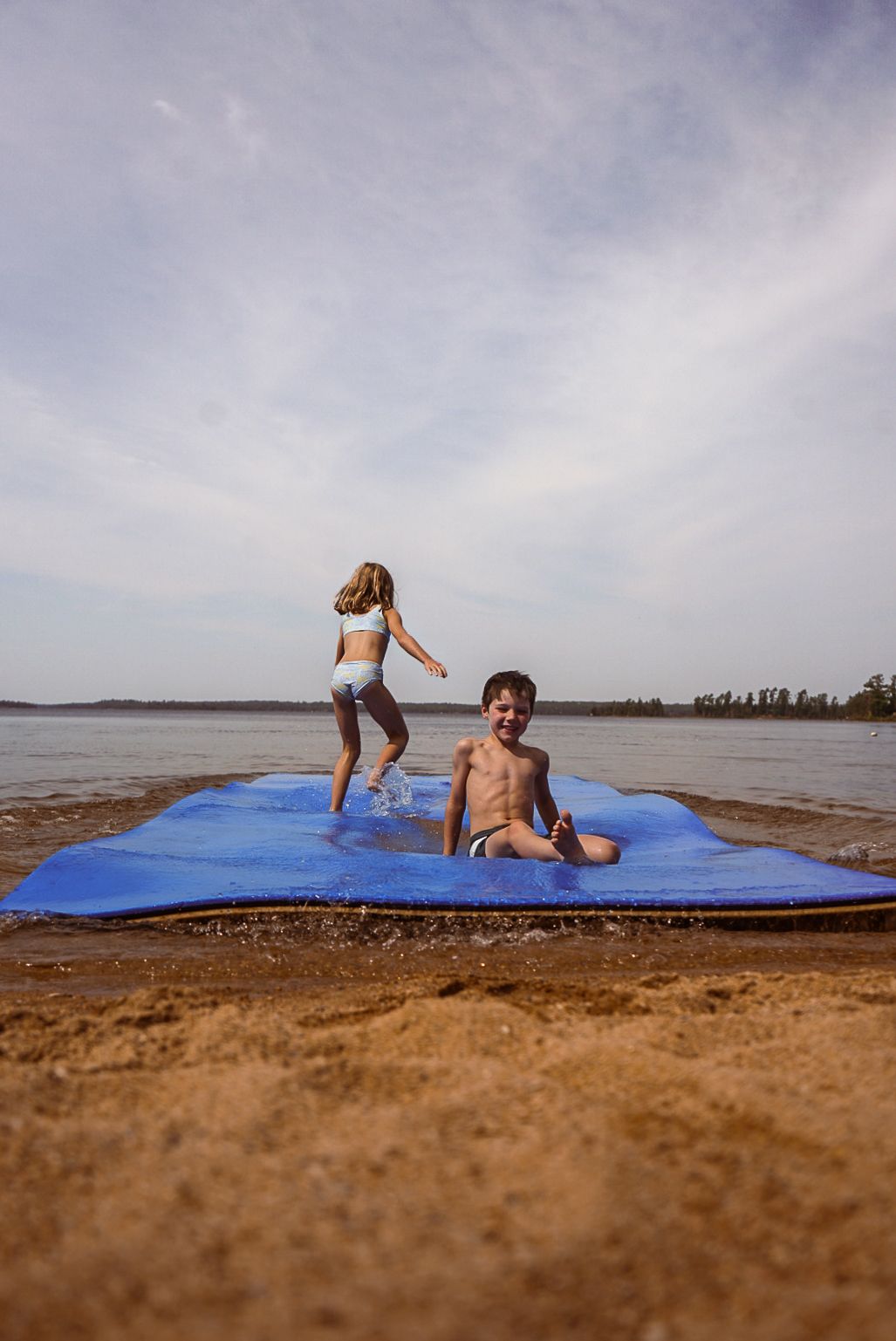 People playing on a blue mat at the beach during a cloudy day.