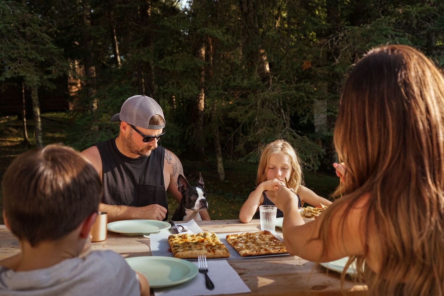 People enjoying a meal together outdoors during sunset at a wooden table.