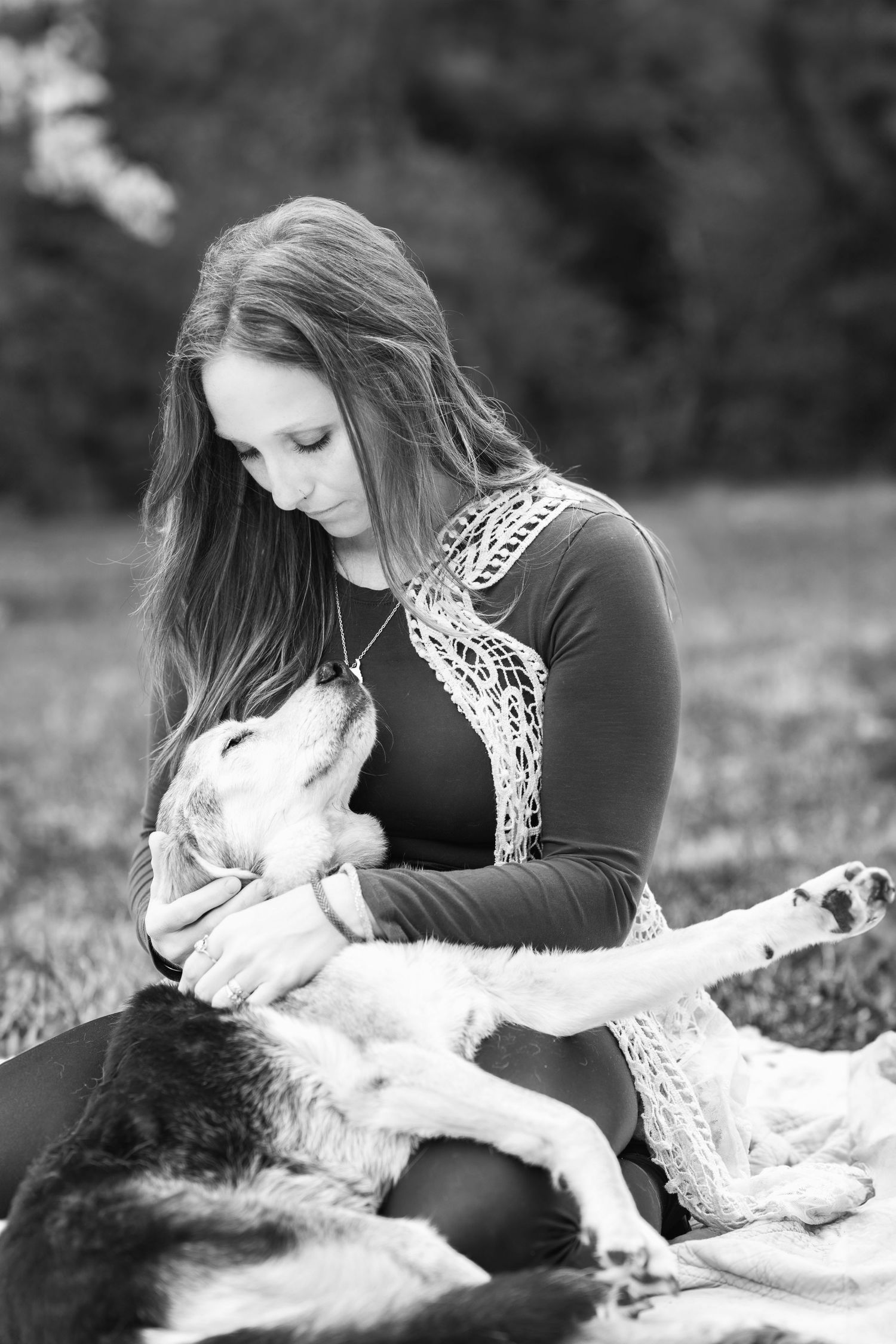 A person in a dark top with lace detail sits outdoors tenderly interacting with a resting black and white dog.