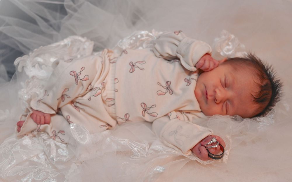 Peaceful newborn baby sleeping in a white lace outfit on a soft blanket.