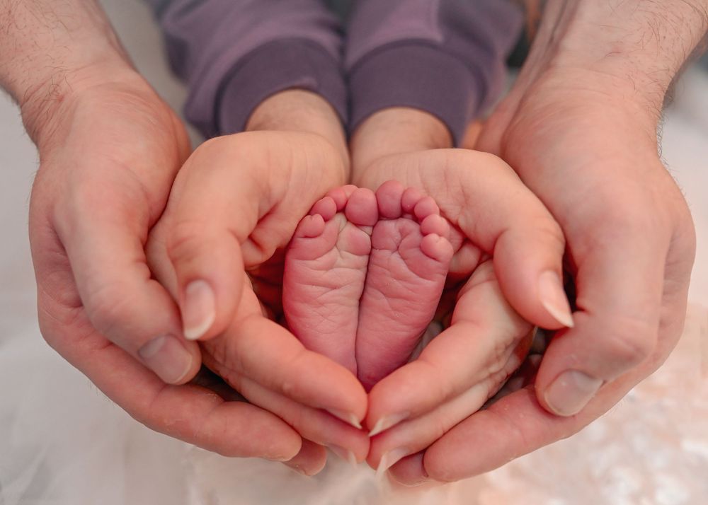 Parents cradling their newborn baby's tiny feet in their hands forming a heart shape.