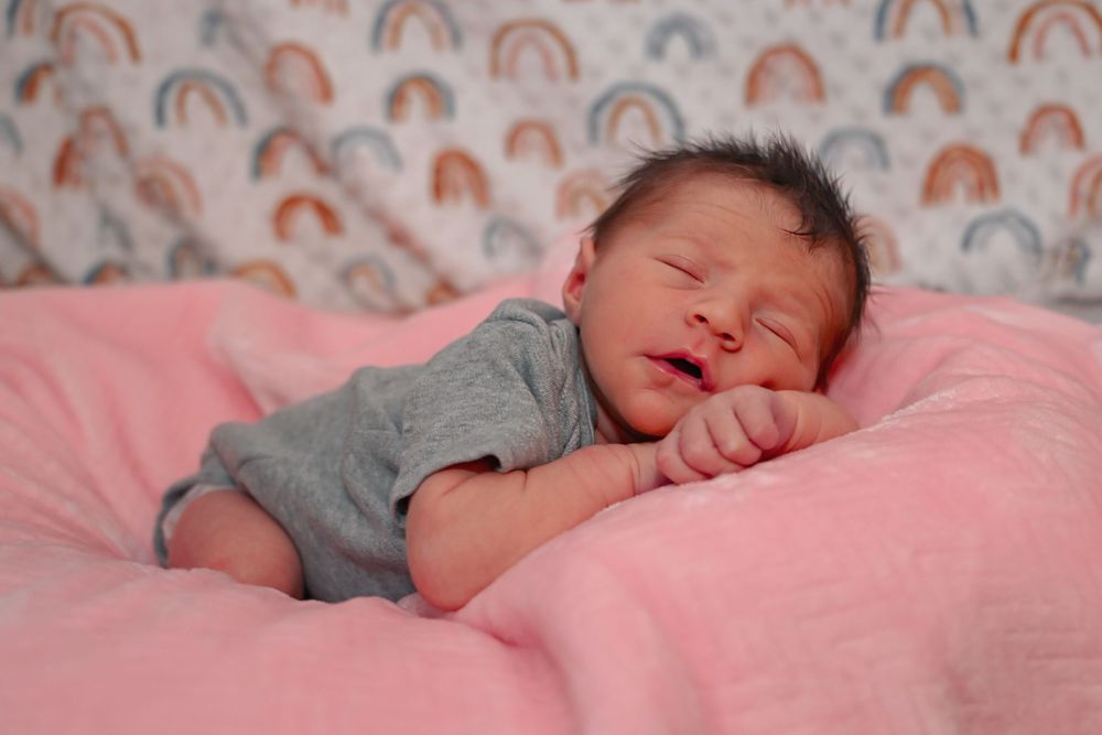 Newborn baby sleeping on a pink blanket with a colorful rainbow patterned background.