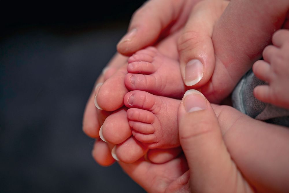 Tiny newborn baby feet cradled gently in loving parents' hands.
