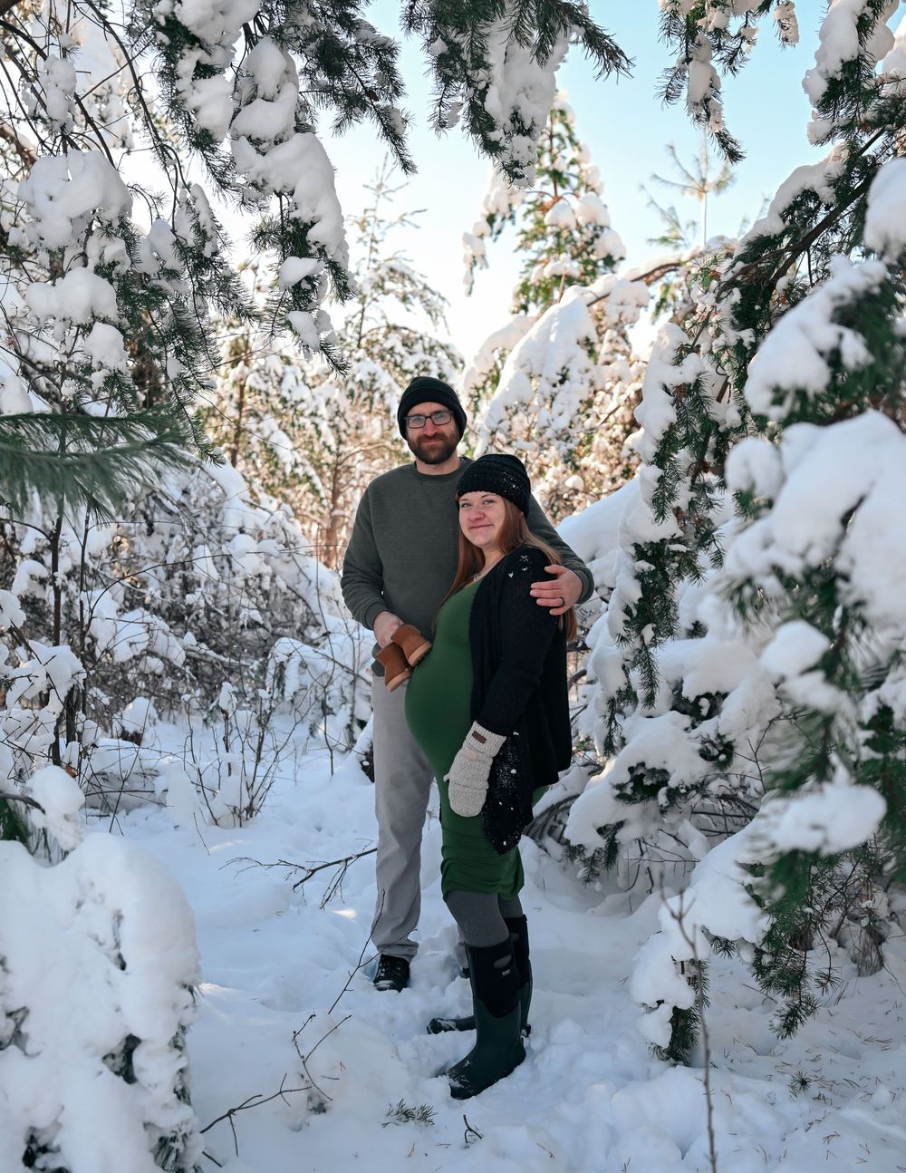 Couple posing together on a snowy winter trail surrounded by snow-covered evergreen trees.