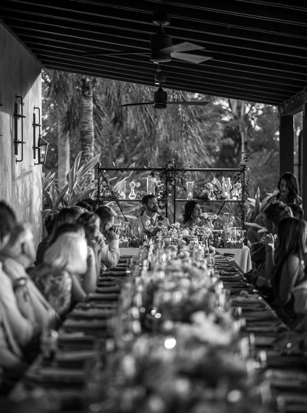 Black and white photo of an elegant wedding reception dinner setup under a covered patio.