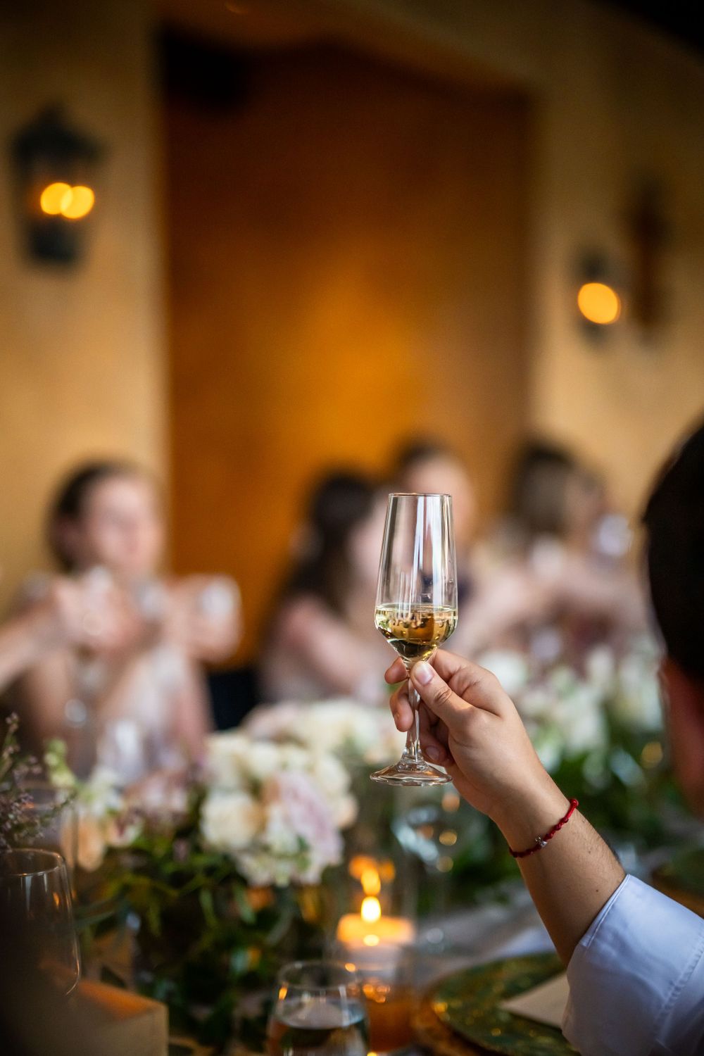 Close-up of hand holding champagne glass at an elegant wedding reception with floral centerpieces.