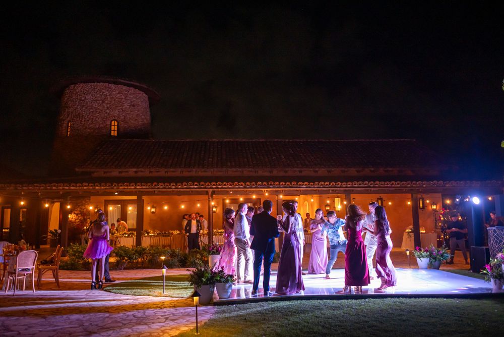Nighttime outdoor wedding reception with guests illuminated by spotlights.