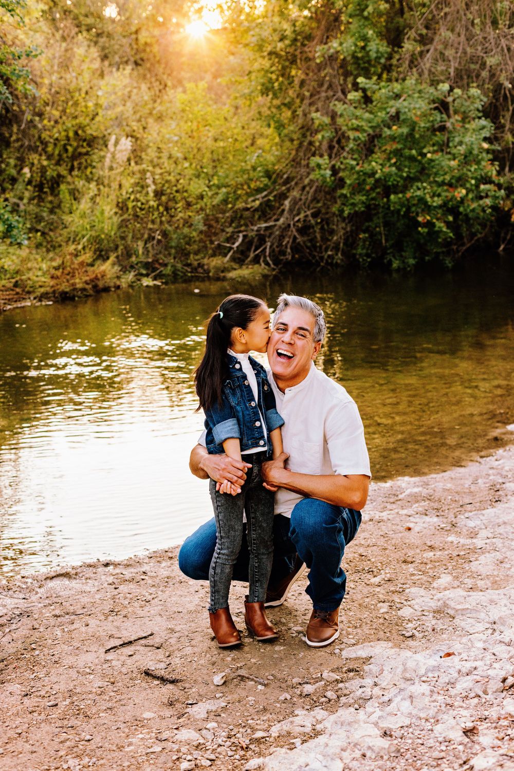 Two people share a joyful moment together by a sunlit river bank during golden hour.