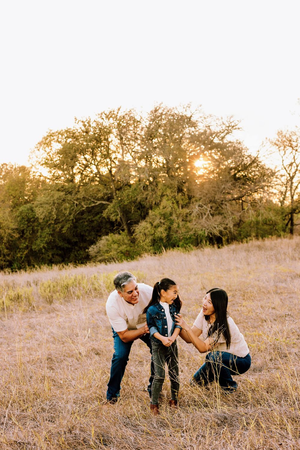 A family shares a tender moment together in a sunlit field of golden grass at sunset.