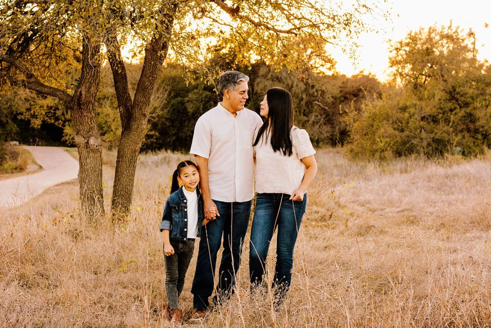 A family stands in a golden sunlit field with trees during sunset creating a warm autumn atmosphere.